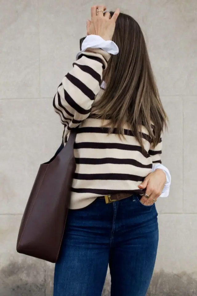 Woman wearing sweater with a belt and jeans and a big bag